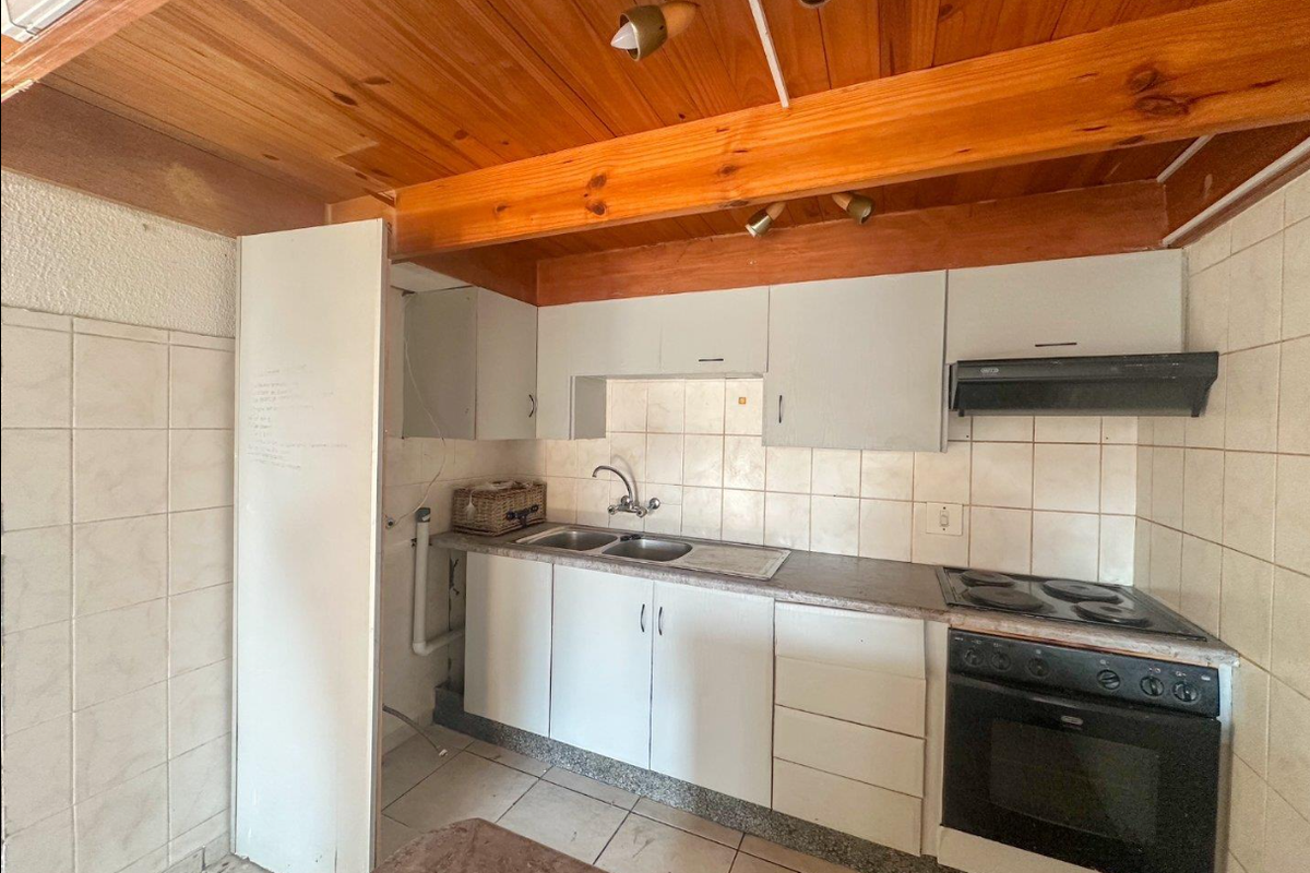 Compact kitchen featuring built-in cabinetry, electric stove with extractor fan, tiled backsplash, and exposed timber ceiling beams.