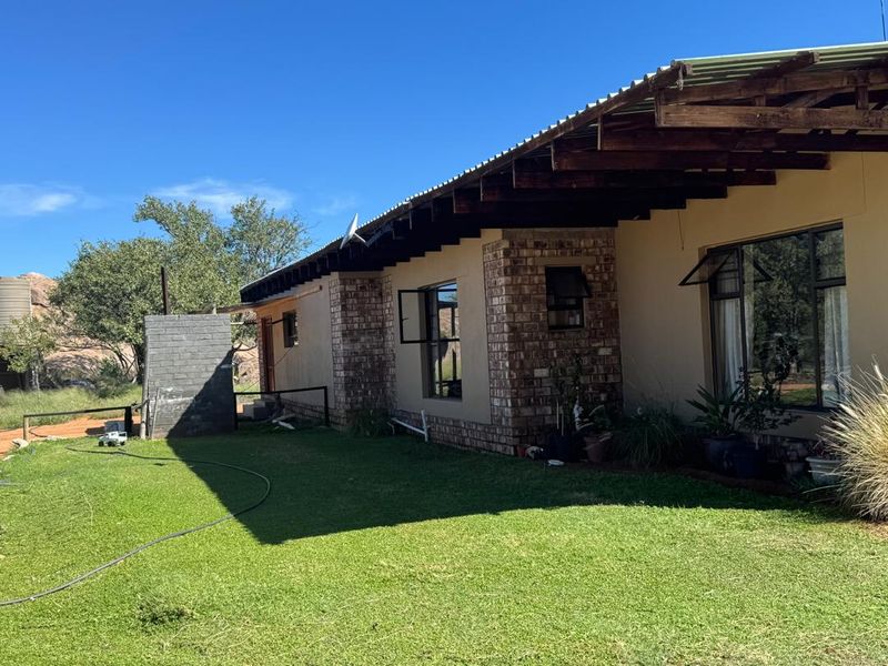 Rear view of the farm dwelling featuring exposed timber rafters, corrugated metal roofing, and face brick accents set against a landscaped garden.