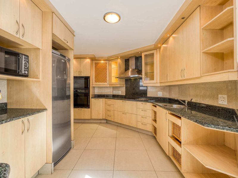 A well-maintained kitchen featuring light-wood cabinetry, granite countertops, built-in oven, stainless steel extractor fan, and tiled flooring.