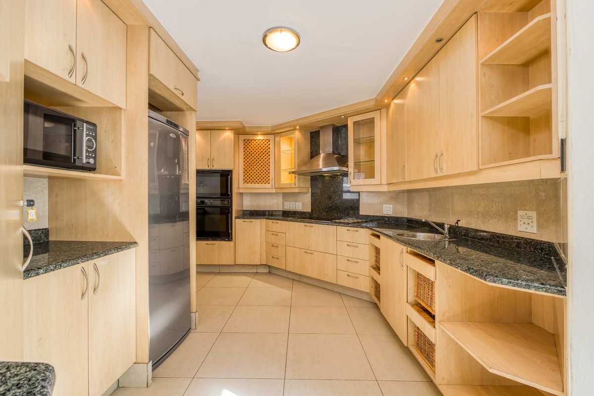 A well-maintained kitchen featuring light-wood cabinetry, granite countertops, built-in oven, stainless steel extractor fan, and tiled flooring.
