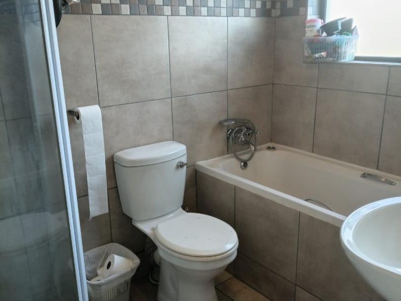 A functional bathroom featuring a shower enclosure, bathtub, toilet, and basin with neutral wall and floor tiling.