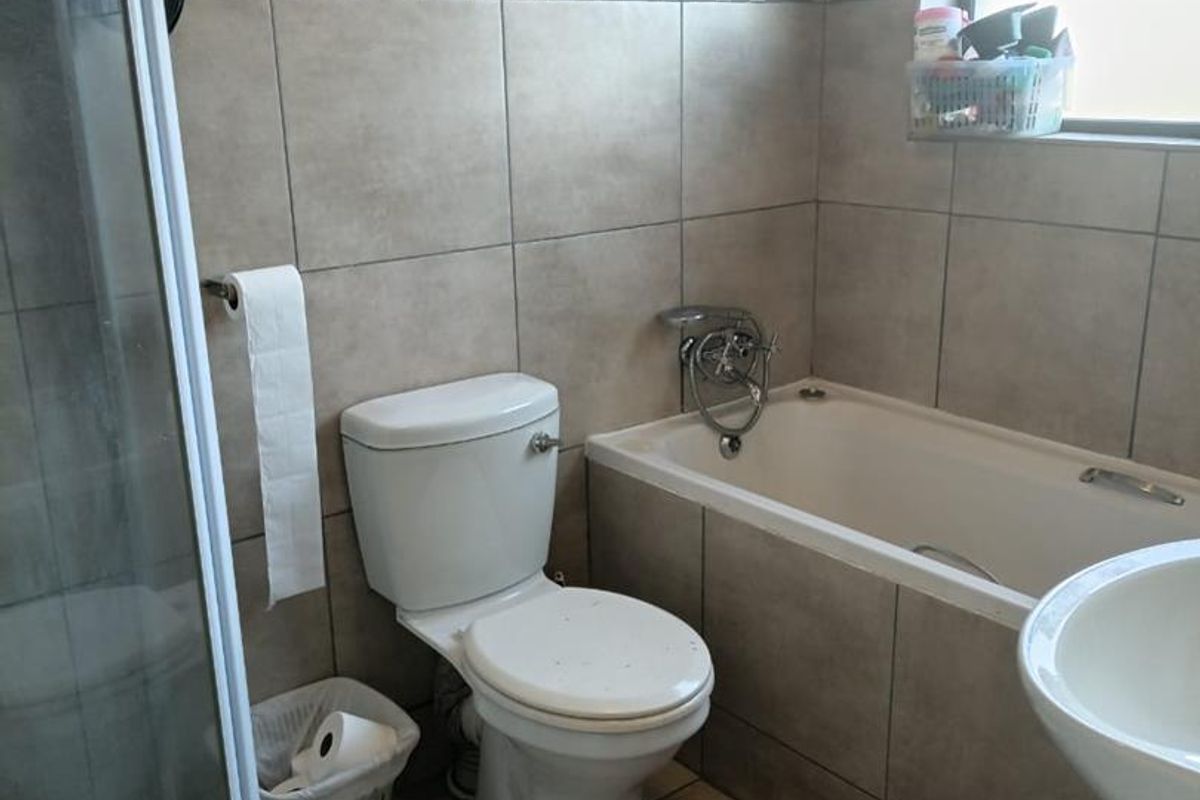 A functional bathroom featuring a shower enclosure, bathtub, toilet, and basin with neutral wall and floor tiling.