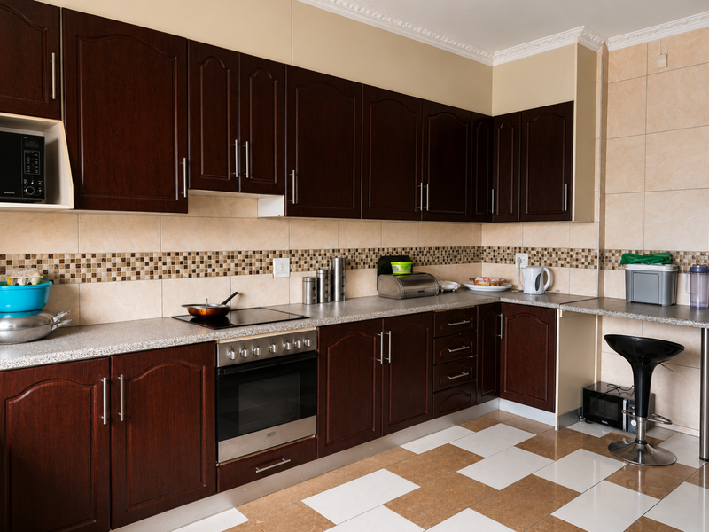 A functional kitchen featuring dark wood cabinetry, laminate countertops, a built-in oven with electric cooktop, and a decorative tiled backsplash.