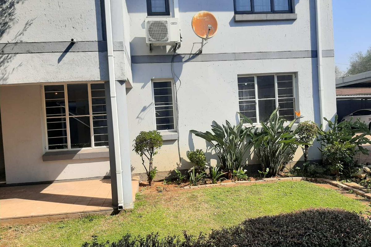Rear view of the townhouse featuring a small tiled patio, landscaped garden, and exterior wall finishes with visible signs of wear.