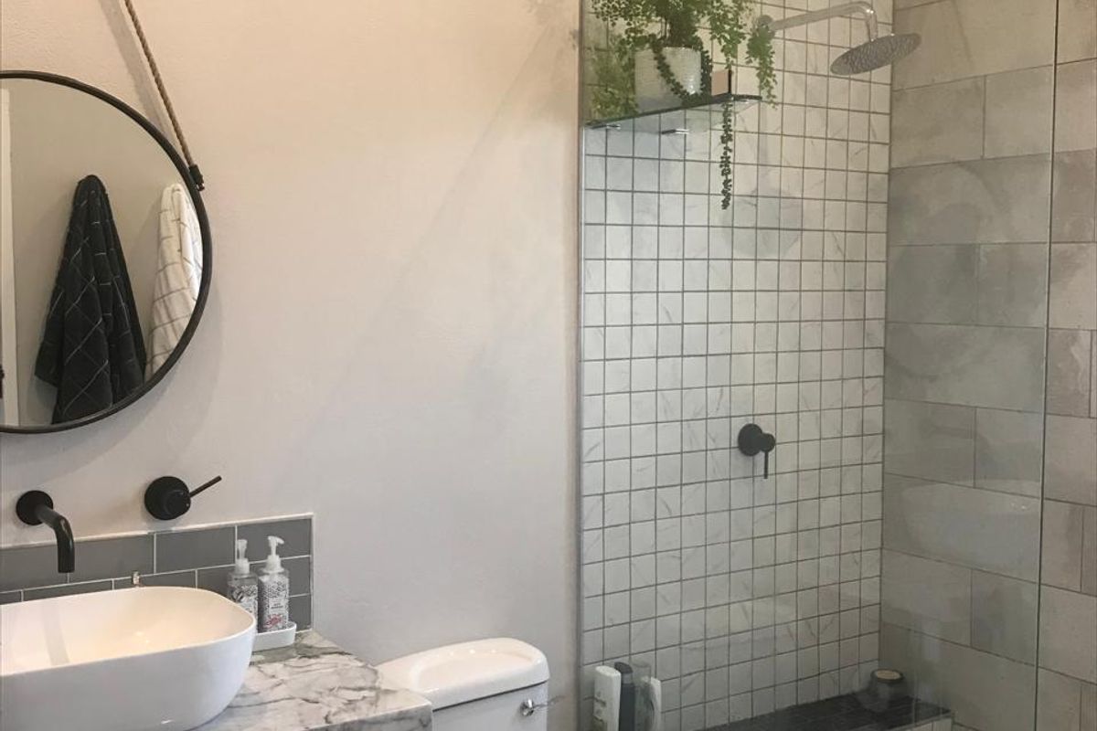 Modern bathroom featuring a marble-topped vanity with a vessel sink, wall-mounted fixtures, and a spacious walk-in shower with contemporary tiling and a glass screen.