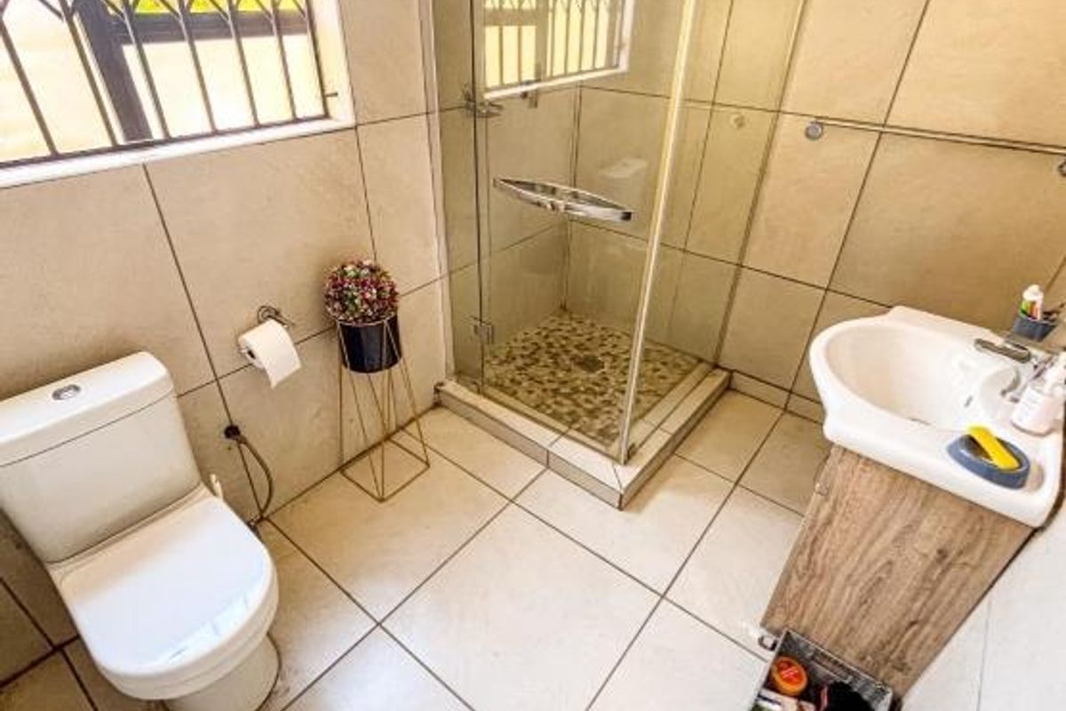 A functional bathroom featuring a glass-enclosed shower, a pedestal vanity with integrated basin, and a standard toilet, finished with neutral wall and floor tiles.