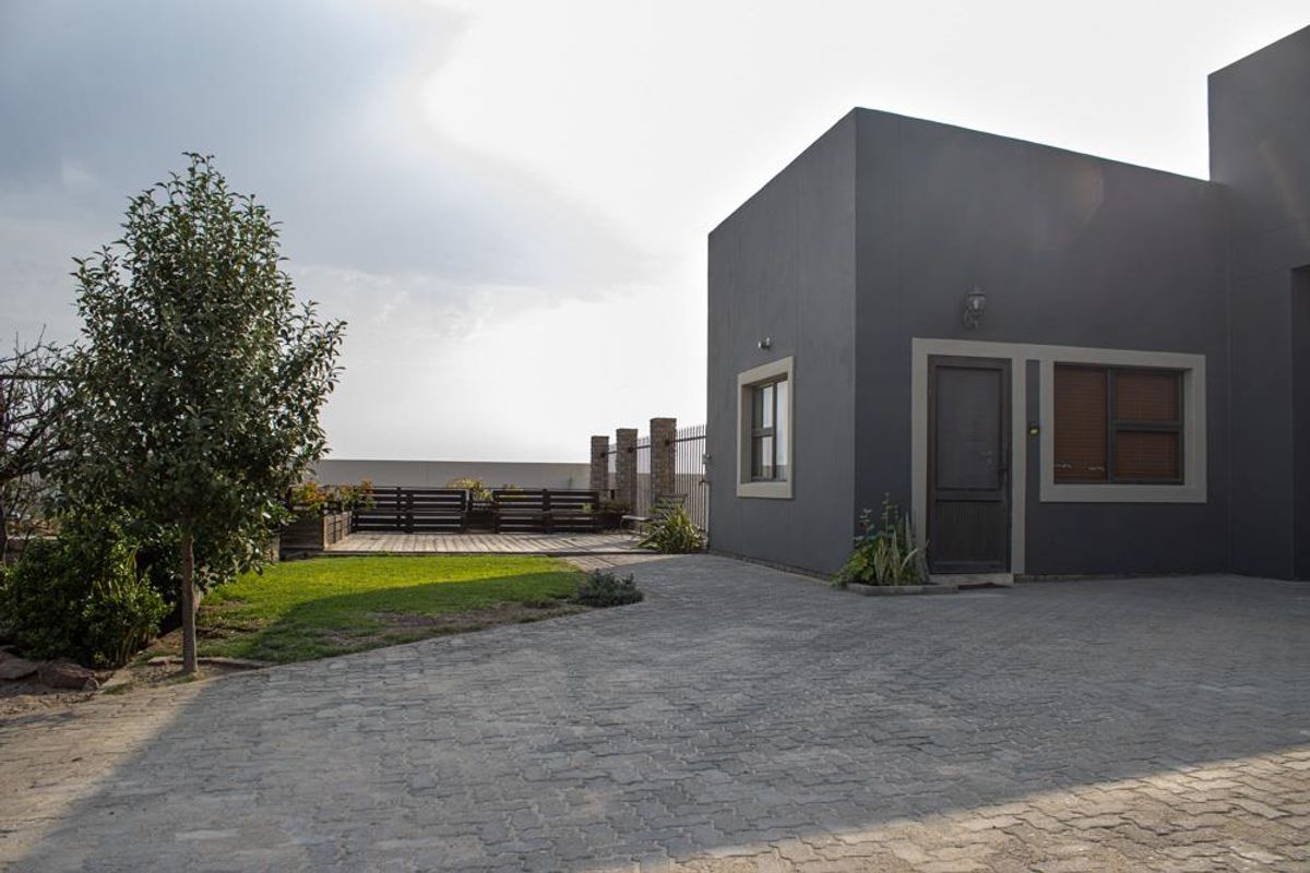 Modern exterior view of the property featuring a paved driveway, landscaped garden area, and a raised timber deck with perimeter fencing.