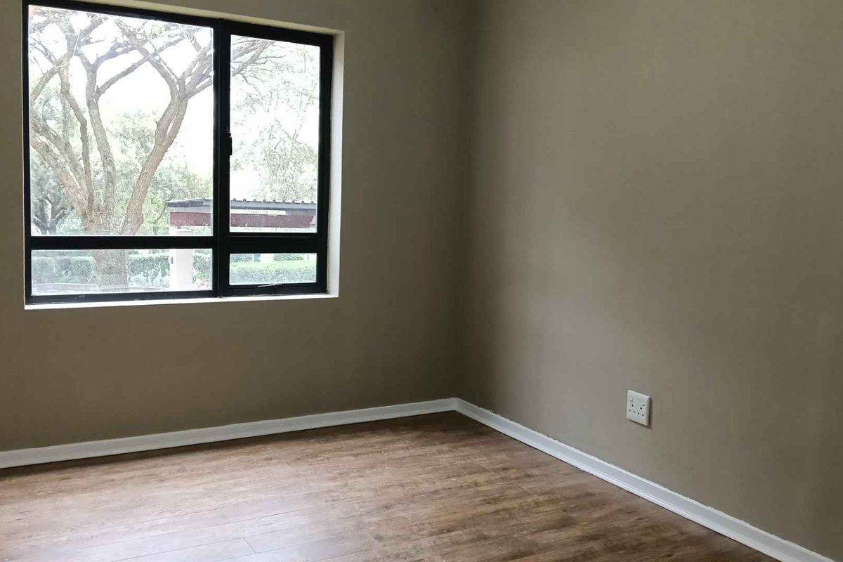 A bright and empty bedroom featuring modern laminate flooring, neutral wall tones, and a large black aluminium window frame.