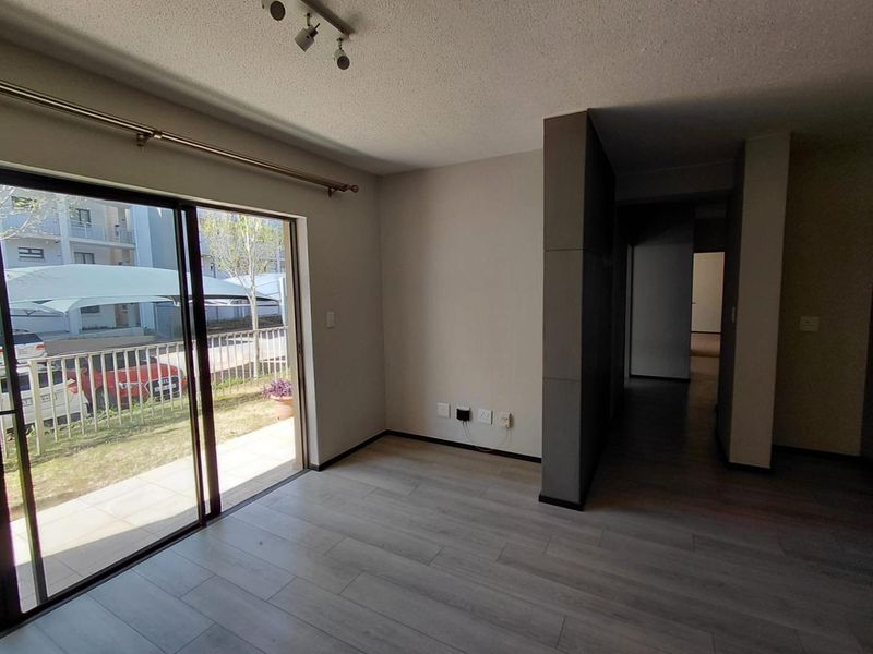 Bright and spacious living area featuring modern laminate flooring, track lighting, and a large sliding glass door leading to an outdoor patio area.