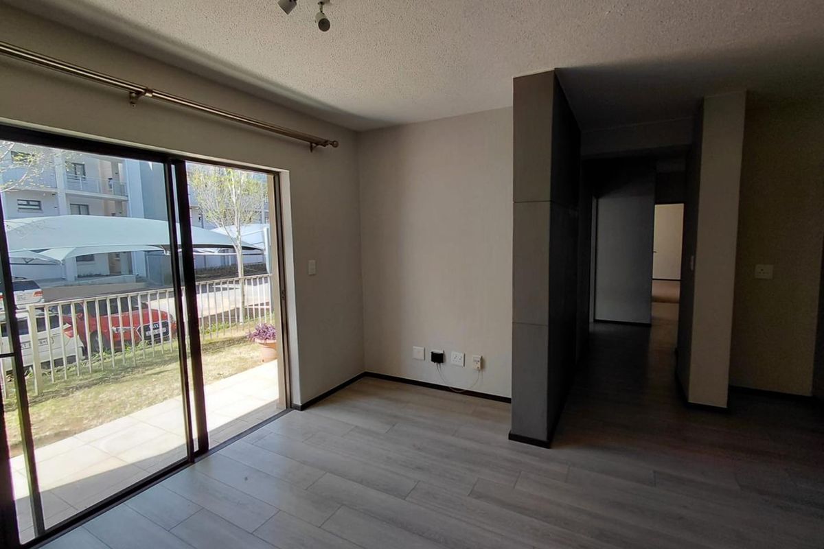 Bright and spacious living area featuring modern laminate flooring, track lighting, and a large sliding glass door leading to an outdoor patio area.