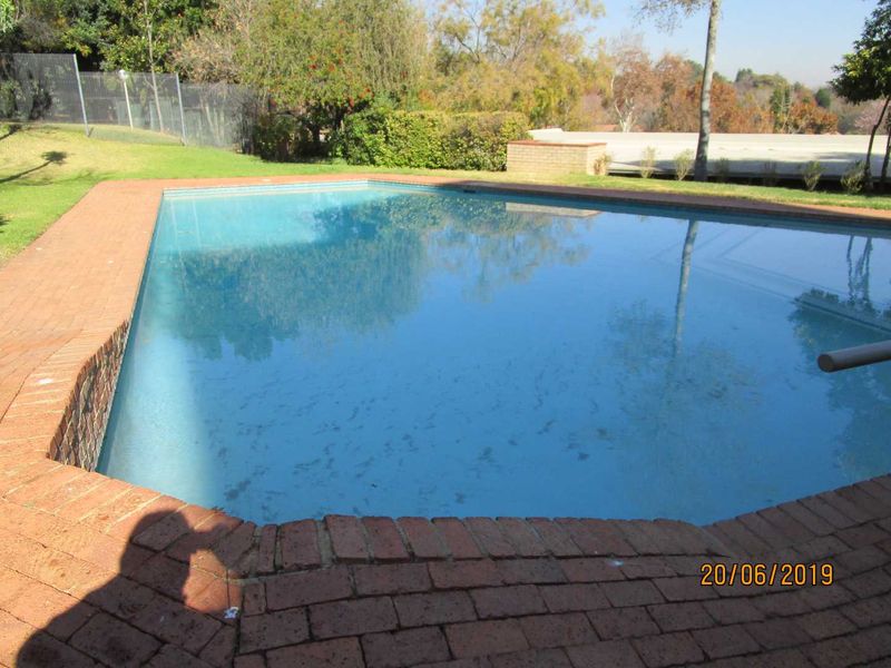 A residential swimming pool featuring brick coping, set within a landscaped garden area with perimeter fencing.