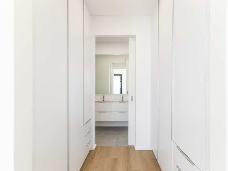A clean, modern hallway featuring extensive built-in cabinetry and a sliding door leading into a bright, contemporary bathroom.