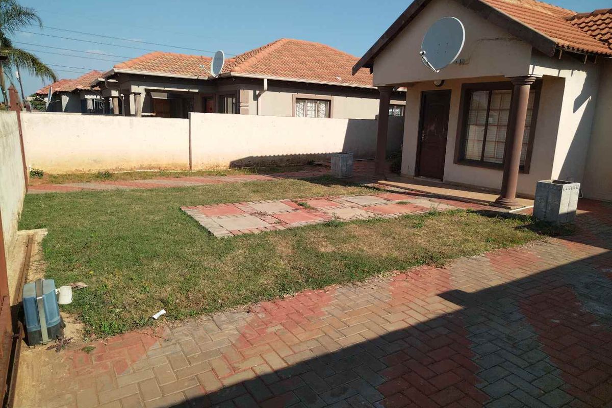 A rear view of the house featuring a paved patio area, a small lawn, and perimeter boundary walls.
