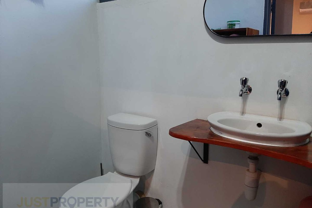 A functional bathroom featuring a white toilet, a wall-mounted basin with a wooden shelf vanity, and a simple mirror.