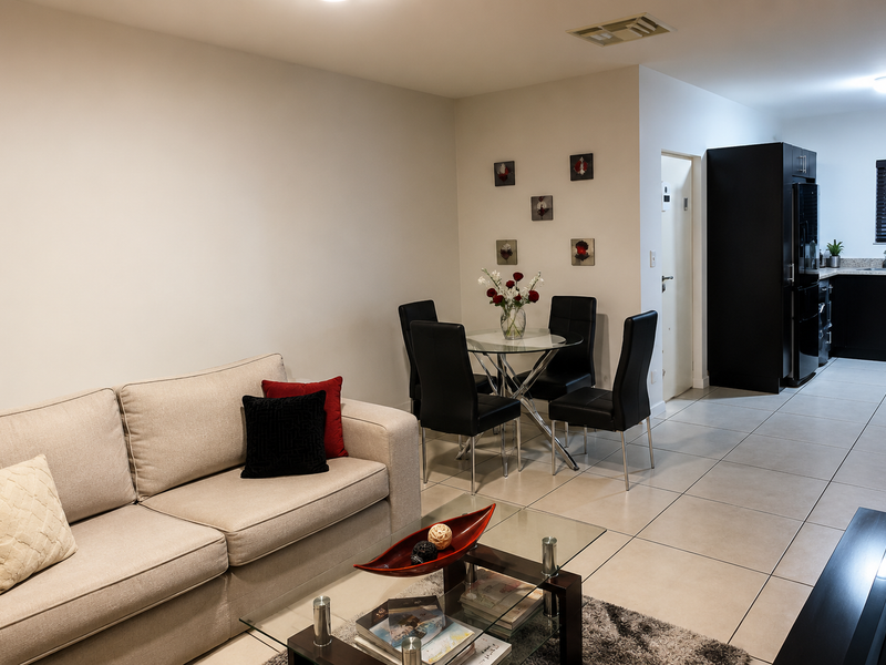 An open-plan living and dining area featuring neutral tiled flooring, recessed lighting, and a modern kitchen with dark cabinetry.
