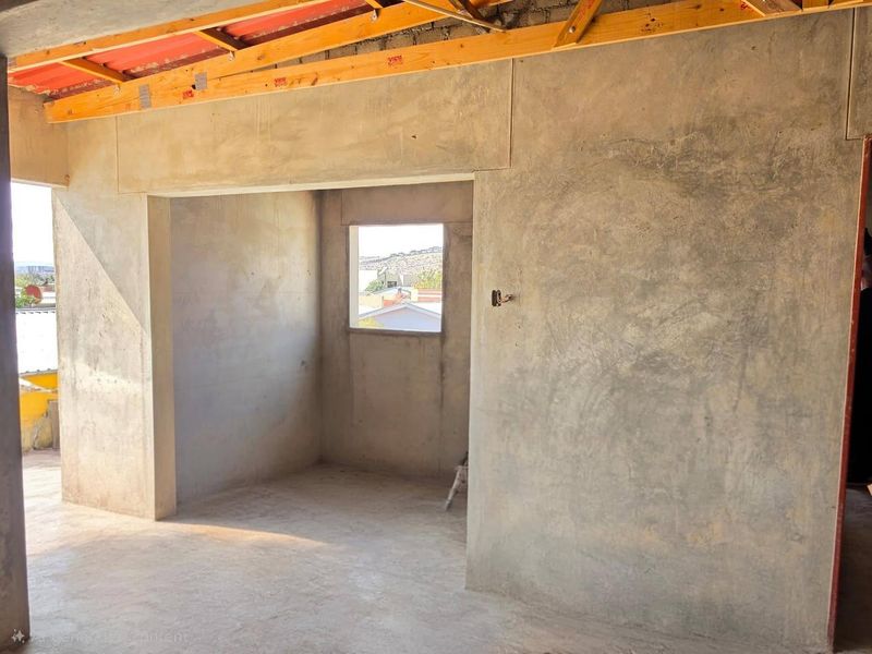 An unfinished bedroom space featuring exposed timber roof trusses, raw plastered walls, and cement flooring, awaiting final interior finishes and ceiling installation.