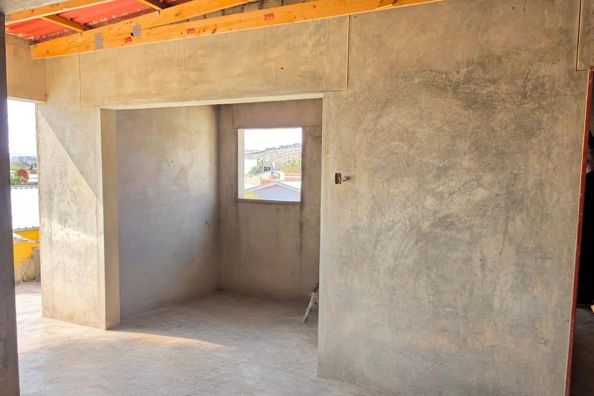An unfinished bedroom space featuring exposed timber roof trusses, raw plastered walls, and cement flooring, awaiting final interior finishes and ceiling installation.