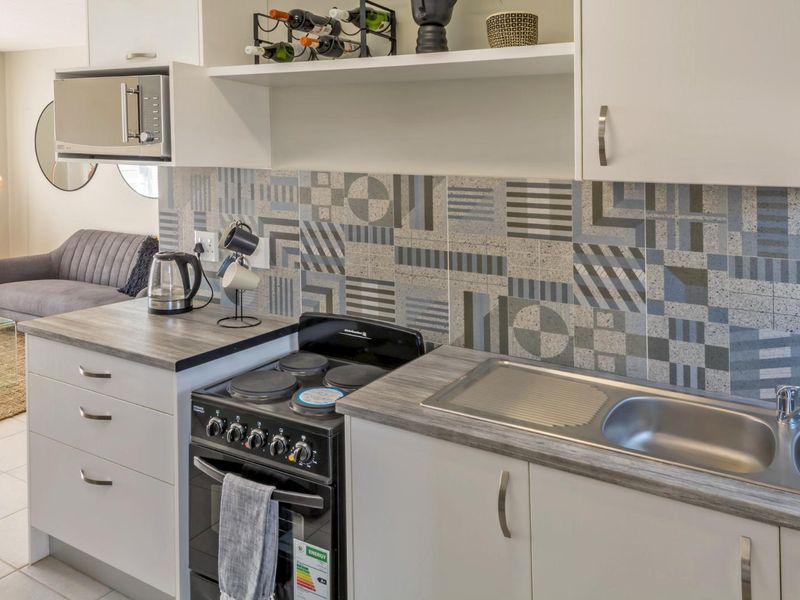 A compact, modern kitchen featuring white cabinetry, a wood-look laminate countertop, a stainless steel sink, and a patterned tile backsplash.