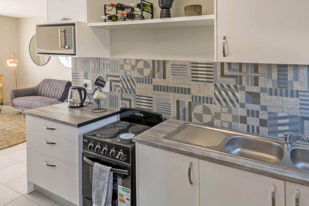 A compact, modern kitchen featuring white cabinetry, a wood-look laminate countertop, a stainless steel sink, and a patterned tile backsplash.