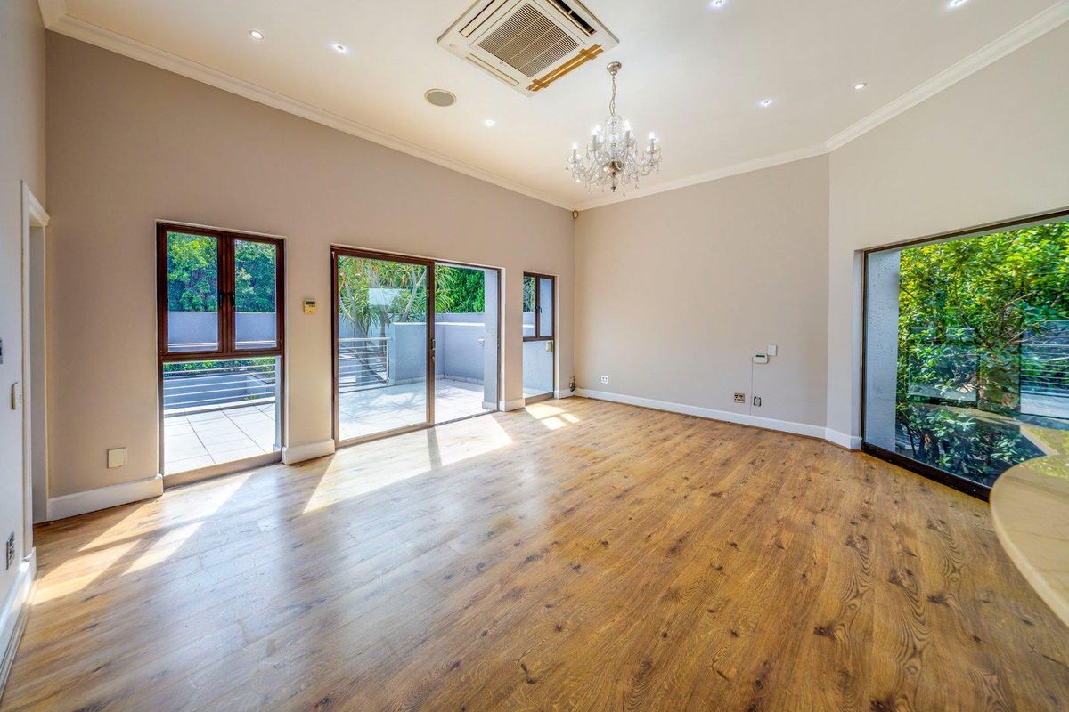 Spacious living area featuring wood-look flooring, recessed ceiling lighting, a central chandelier, and large sliding glass doors providing access to an outdoor patio.