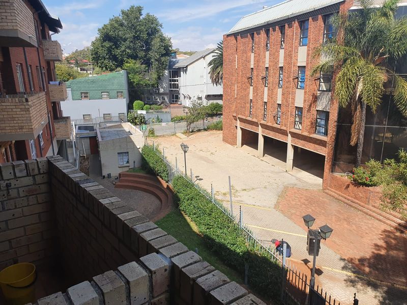 View from a balcony overlooking a shared brick-paved courtyard, security fencing, and adjacent apartment building structures.