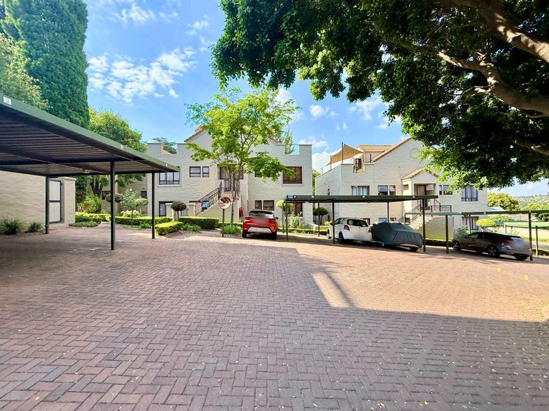 Exterior view of the apartment complex featuring paved parking areas, covered carports, and landscaped garden surroundings.