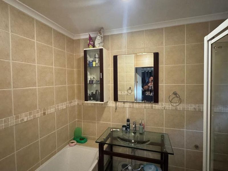 A functional bathroom featuring a built-in bathtub, glass vanity basin, wall-mounted storage cabinet, and a separate shower enclosure with neutral wall tiling.