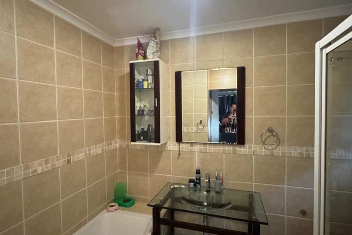 A functional bathroom featuring a built-in bathtub, glass vanity basin, wall-mounted storage cabinet, and a separate shower enclosure with neutral wall tiling.