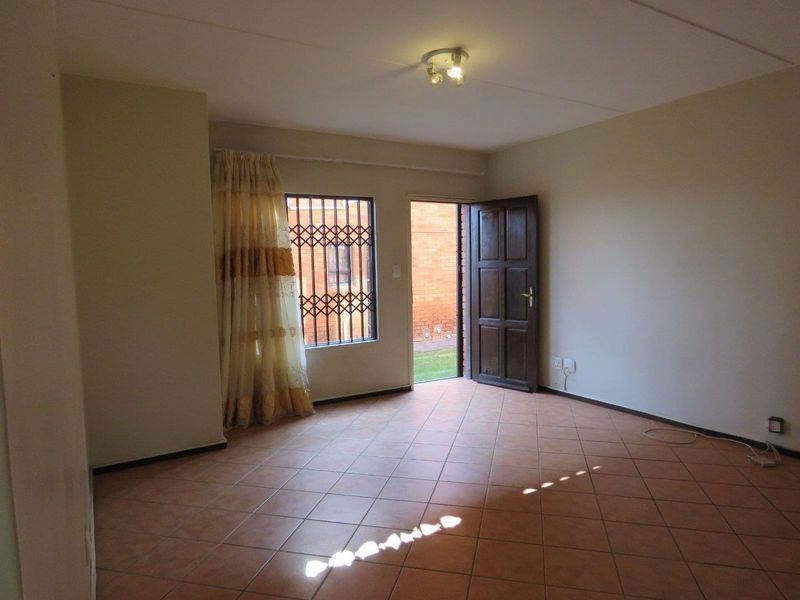 An empty living room featuring tiled flooring, a ceiling light fixture, and a door leading to an outdoor area with security bars.