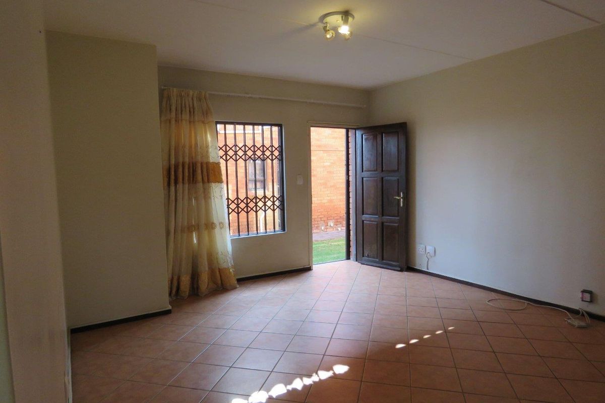 An empty living room featuring tiled flooring, a ceiling light fixture, and a door leading to an outdoor area with security bars.