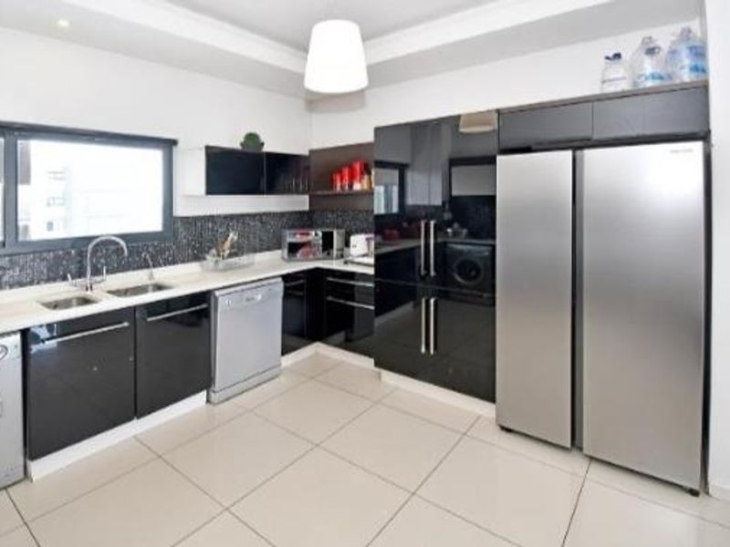 Modern kitchen featuring high-gloss black cabinetry, mosaic tile backsplash, integrated appliances, and large format floor tiles in a clean, contemporary layout.