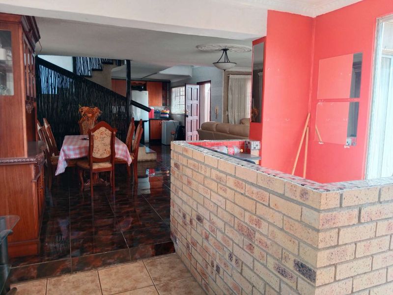 Open plan living and dining area featuring a brick partition wall, tiled flooring, and an integrated staircase leading to the upper level.
