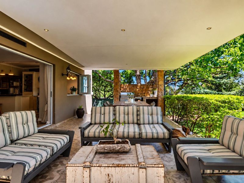 Covered outdoor patio featuring a built-in braai with stone cladding, recessed lighting, and tiled flooring, providing seamless access to the garden.