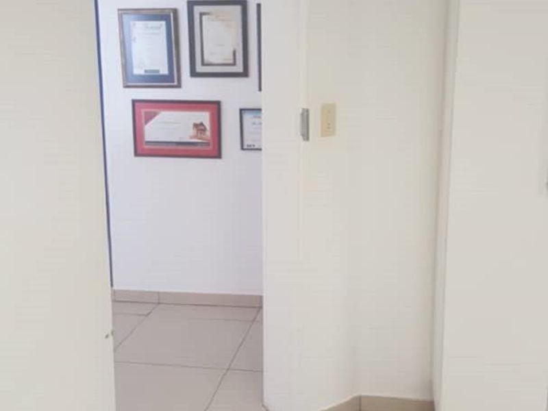 A bright, tiled hallway connecting office spaces, featuring a transom window above the doorway and built-in storage cabinetry.
