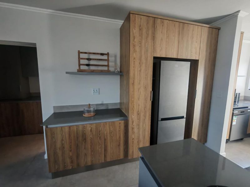 Modern kitchen area featuring wood-grain cabinetry, dark stone countertops, and a dedicated integrated fridge housing unit.