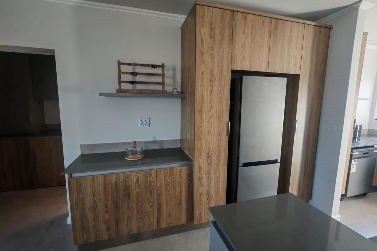 Modern kitchen area featuring wood-grain cabinetry, dark stone countertops, and a dedicated integrated fridge housing unit.