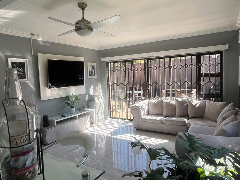 A bright and modern living room featuring large format floor tiles, a ceiling fan, and sliding glass doors with security gates leading to the patio.