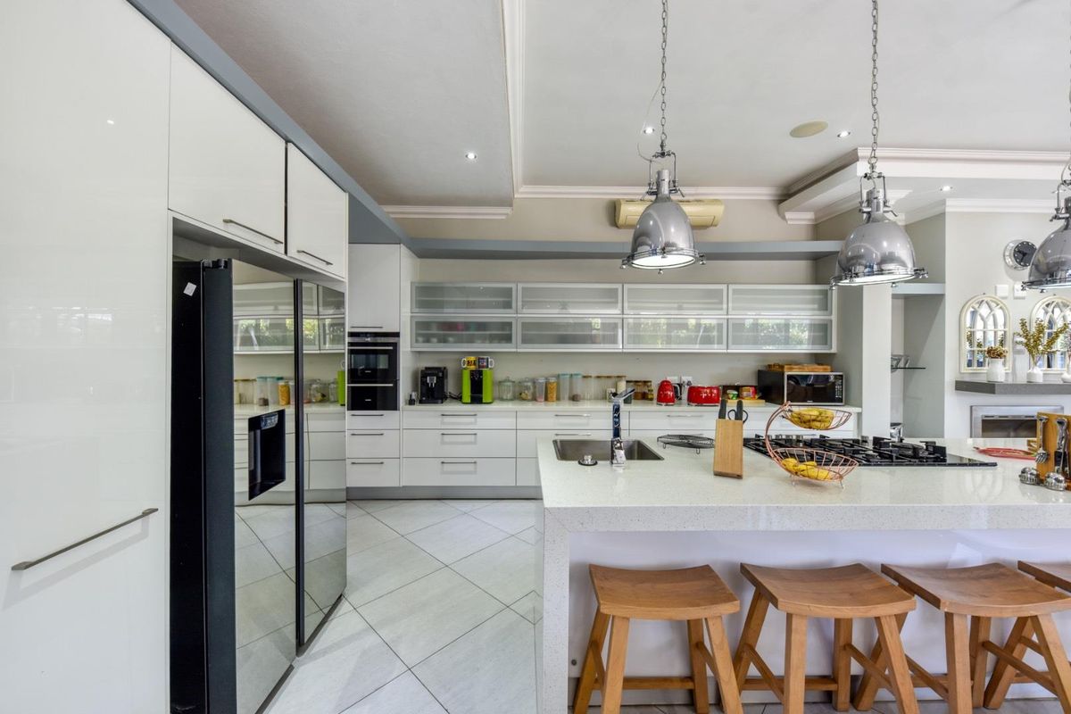 Modern kitchen featuring white cabinetry, stone countertops, a central island with a gas hob, and industrial-style pendant lighting.