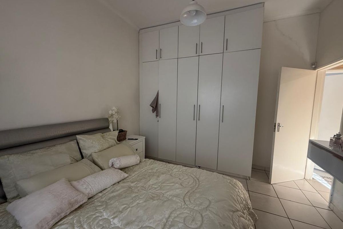 A bedroom featuring floor-to-ceiling built-in wardrobes, tiled flooring, and a central pendant light fixture.