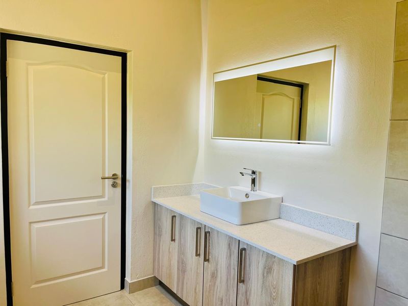 Modern bathroom featuring a sleek vanity with a stone countertop, vessel sink, chrome faucet, and a contemporary backlit mirror.