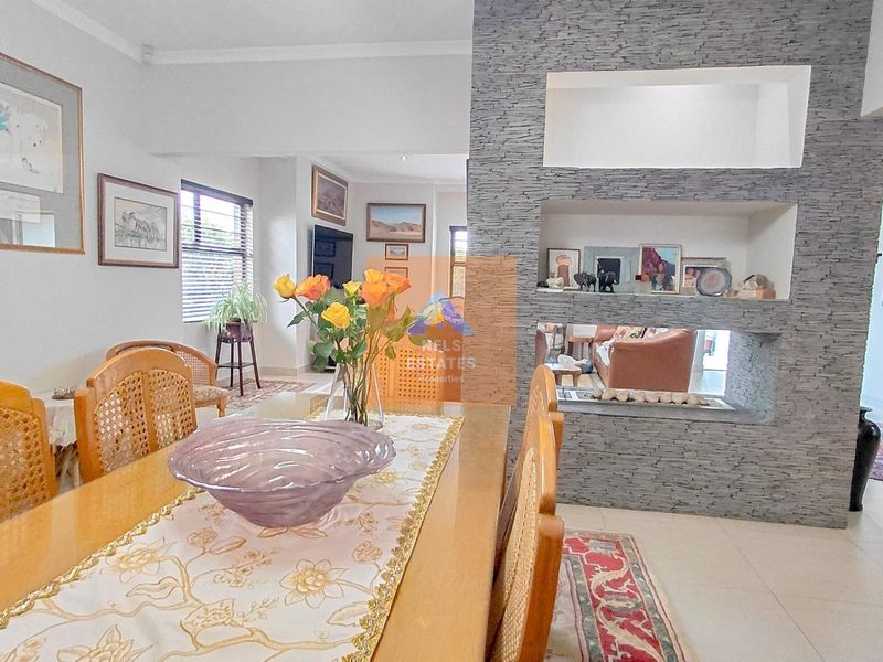 Dining area featuring a prominent stone-clad feature wall with a built-in fireplace, connecting to the adjacent living space with neutral tiled flooring.