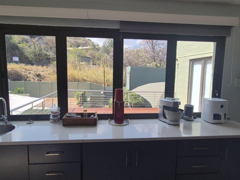 Modern kitchen area featuring dark cabinetry, white quartz countertops, an undermount sink, and large windows overlooking the outdoor terrace.