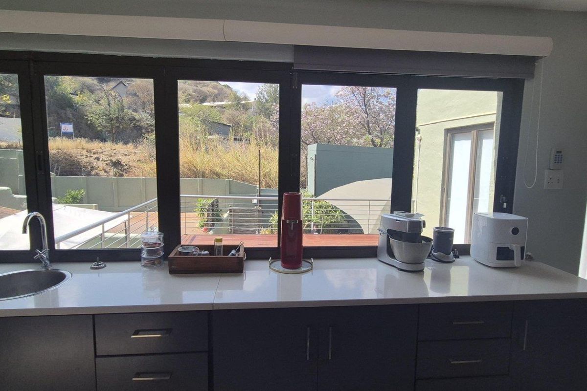 Modern kitchen area featuring dark cabinetry, white quartz countertops, an undermount sink, and large windows overlooking the outdoor terrace.