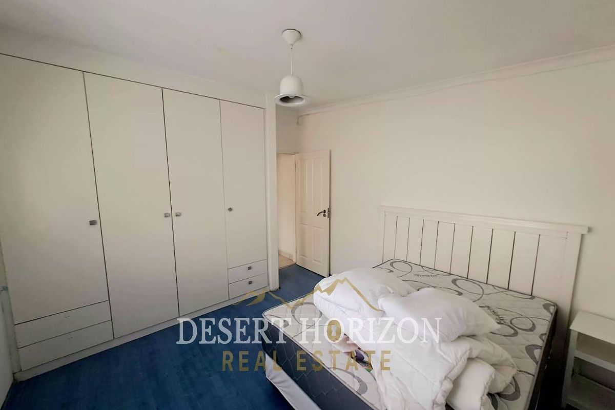 A bedroom featuring built-in wardrobes, laminate flooring, and a pendant light fixture, offering a functional space with neutral wall finishes.