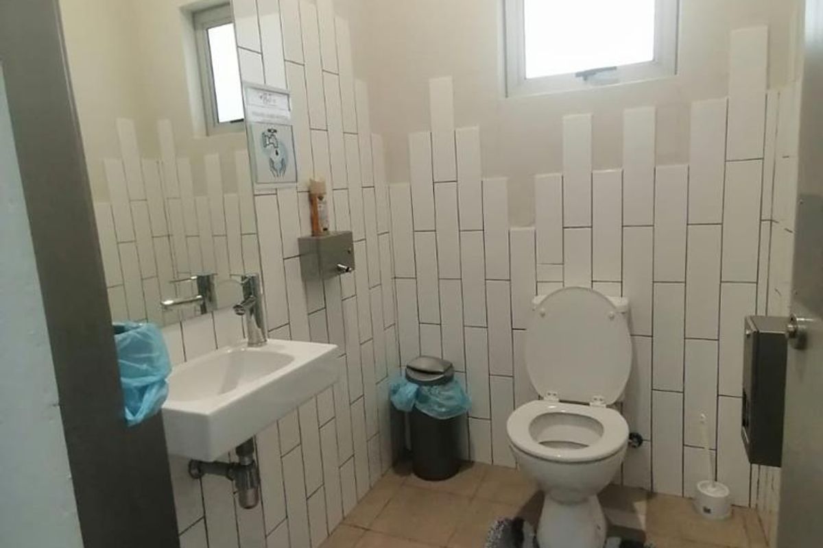 A functional bathroom featuring a wall-mounted basin, toilet, and vertical subway tile backsplash.
