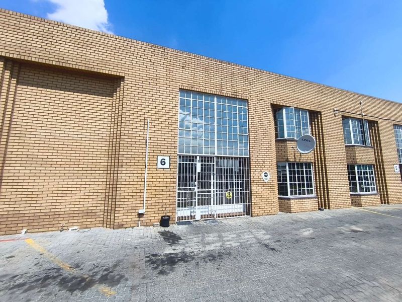 Front elevation of an industrial unit featuring face brick construction, steel-framed windows, and a secure entrance gate with paved driveway access.
