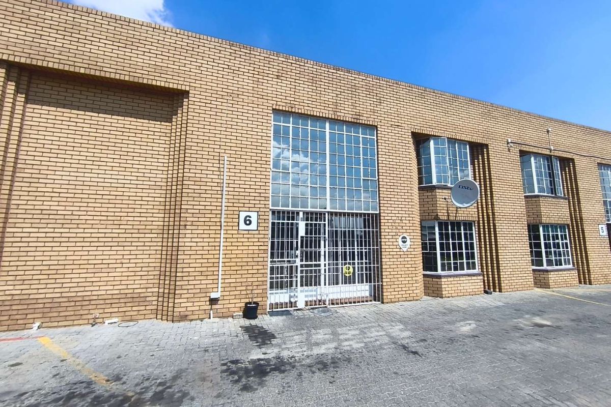 Front elevation of an industrial unit featuring face brick construction, steel-framed windows, and a secure entrance gate with paved driveway access.