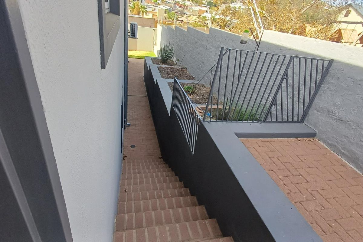 A paved exterior staircase leading down to a side walkway, featuring modern retaining walls, metal safety railings, and raised garden beds.