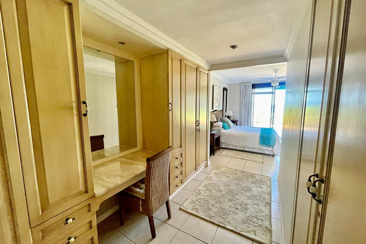 A bedroom featuring built-in wooden cabinetry with an integrated vanity area, leading into a sleeping space with access to a balcony.