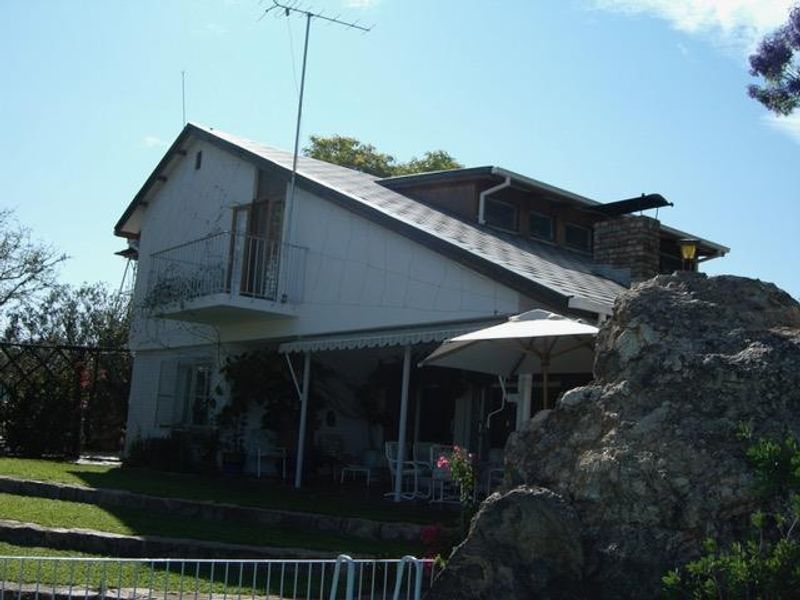 Rear view of a multi-level house featuring a covered patio, a small upper-level balcony, and a prominent brick chimney.